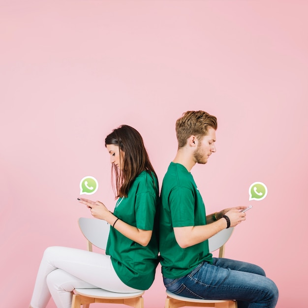 Jeune couple assis dos à dos en utilisant WhatsApp sur smartphone