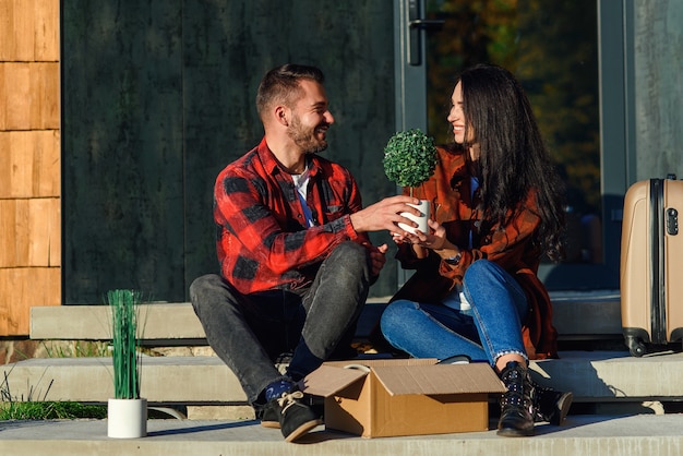 Photo jeune couple assis sur les escaliers s'amusant à déballer les boîtes après avoir déménagé dans une nouvelle maison.