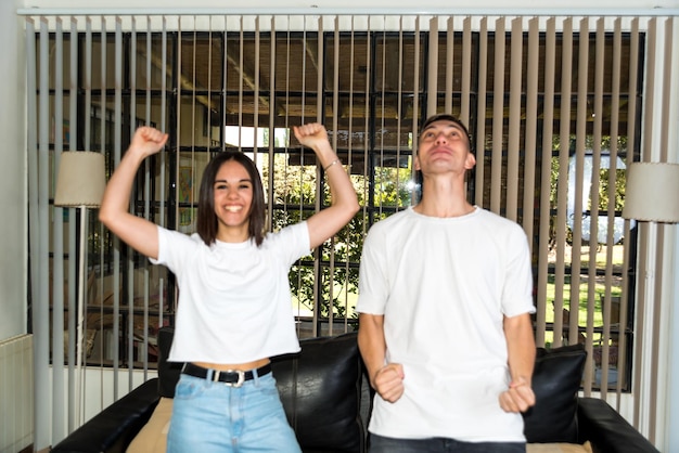 jeune couple assis sur leur canapé à la maison en regardant un match de football