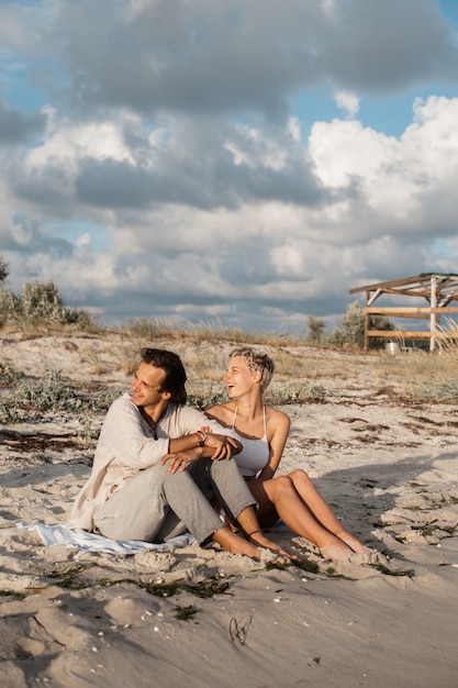 Jeune couple assis sur la plage et souriant