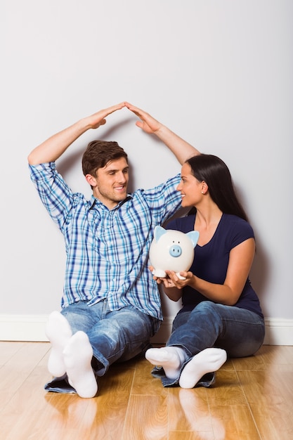 Jeune couple assis sur le plancher avec la tirelire