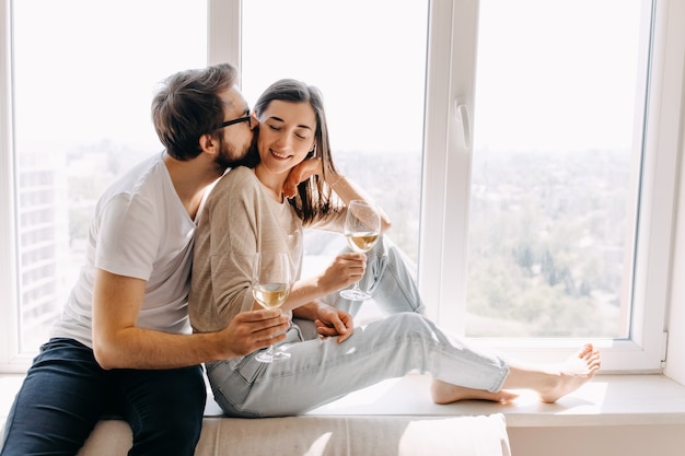 Jeune couple assis sur le rebord de la fenêtre, étreindre et boire du vin