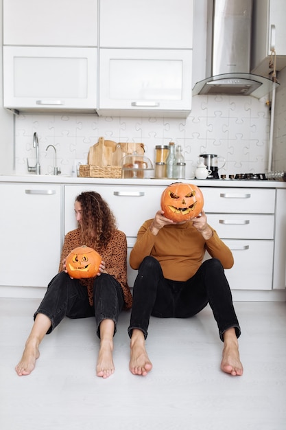 Jeune couple assis sur le sol de la cuisine et tenant des citrouilles d'Halloween