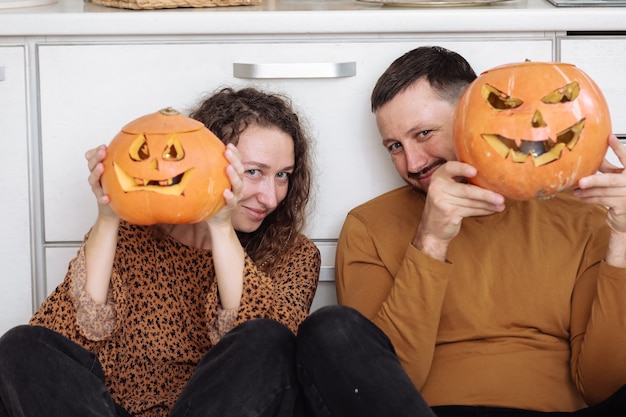 Jeune couple assis sur le sol de la cuisine et tenant des citrouilles d'Halloween