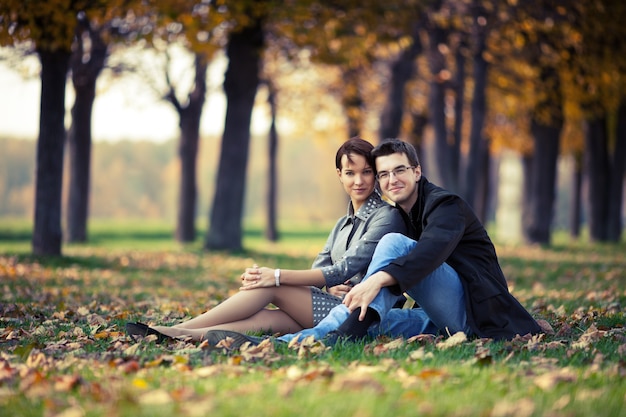 Jeune couple assis sur le sol dans le parc d'automne