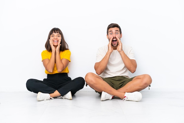 Jeune couple assis sur le sol isolé sur fond blanc criant et annonçant quelque chose