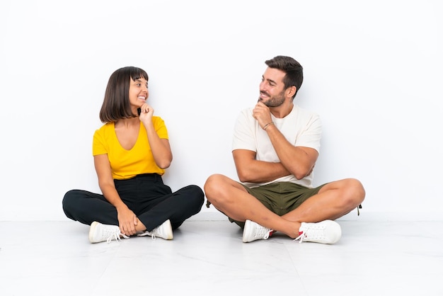 Jeune couple assis sur le sol isolé sur fond blanc regardant les uns les autres