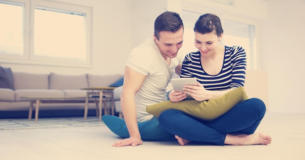 Jeune couple assis sur le sol et utilisant Internet sur tablette numérique