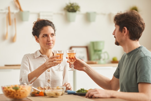 Jeune couple assis à la table et célébrant avec du vin pendant le dîner à la maison