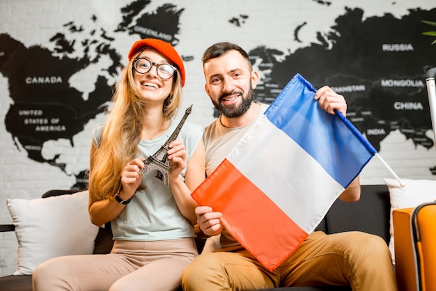 Jeune couple assis avec la tour eiffel et le drapeau français au bureau de l'agence de voyages sur le fond de la carte du monde se préparant pour un voyage à Paris