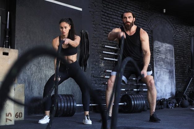 Jeune couple athlétique avec corde de combat faisant de l'exercice dans une salle de fitness d'entraînement fonctionnel.