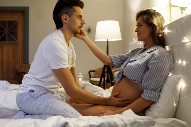 Un jeune couple attend un bébé Le mari et sa femme enceinte se détendent sur le lit