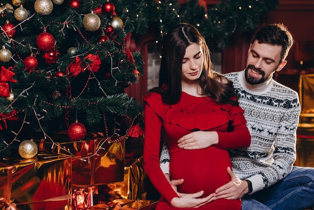 Un jeune couple attend un miracle Un homme et une femme enceinte sur le fond d'un sapin de Noël