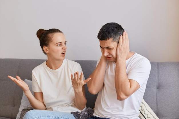 Jeune couple ayant des conflits fureur en colère femme assise sur un canapé et criant sur son mari avec les bras levés ayant des problèmes de querelle dans la relation