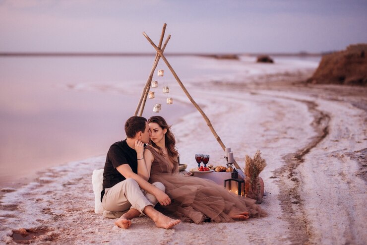 Photo jeune couple ayant un pique-nique sur la plage d'un lac rose