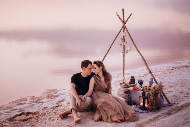 Jeune couple ayant un pique-nique sur la plage d'un lac rose