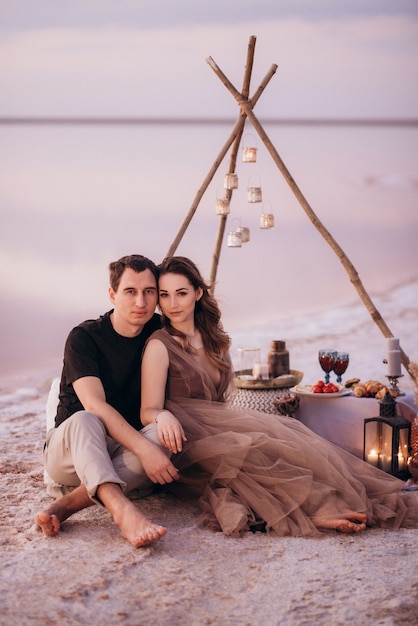 Jeune couple ayant un pique-nique sur la plage d'un lac rose