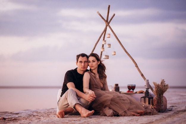 Jeune couple ayant un pique-nique sur la plage d'un lac rose