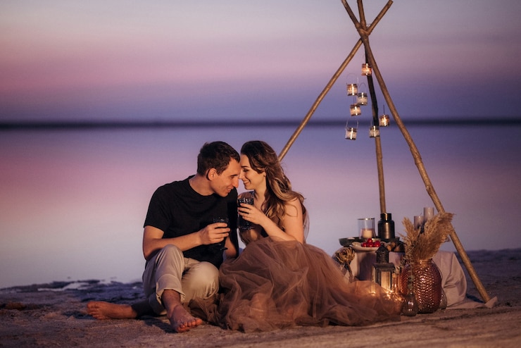 Photo jeune couple ayant un pique-nique sur la plage d'un lac rose
