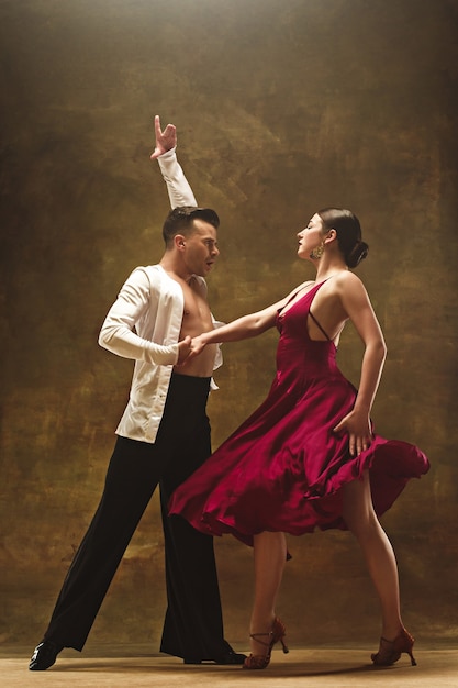 Le jeune couple de bal de danse en robe d'or danse dans une pose sensuelle sur fond de studio. Des danseurs professionnels dansent le tango. Concept de danse de salon. Émotions humaines - amour et passion