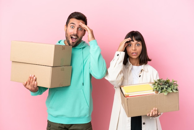 Jeune couple de beauté emménageant dans une nouvelle maison parmi des boîtes isolées sur fond rose vient de réaliser quelque chose et a l'intention de trouver la solution