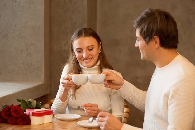 Jeune couple boit du café. Bouquet de roses et cadeau. Rencontres Saint-Valentin.