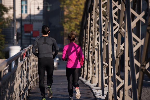 Photo jeune couple en bonne santé faisant du jogging dans la ville tôt le matin avec le lever du soleil en arrière-plan