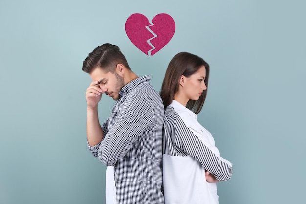Jeune couple bouleversé et illustration du cœur brisé sur fond de couleur Problèmes relationnels