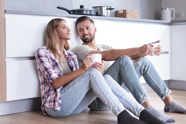 Jeune couple buvant du café assis sur le sol de la cuisine