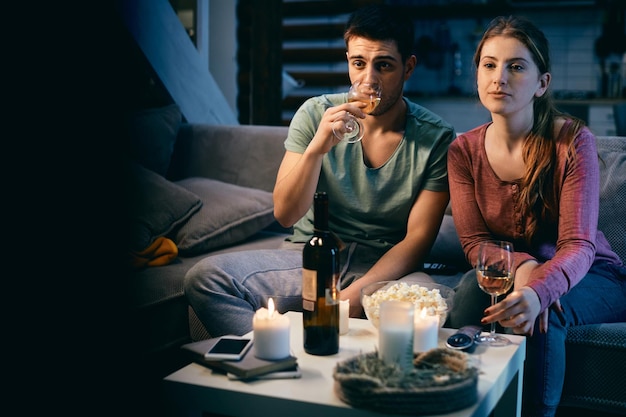 Jeune couple buvant du vin en regardant la télévision la nuit à la maison