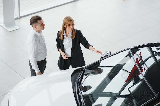 Jeune couple byuing une voiture dans une salle d'exposition de voiture