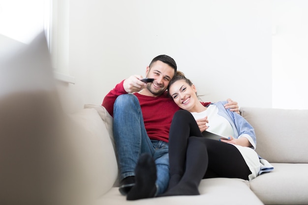 Jeune couple sur le canapé à regarder la télévision ensemble dans leur maison de luxe