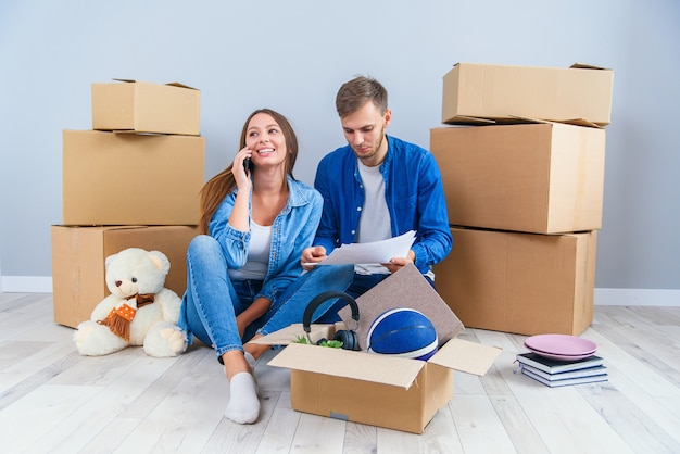 Jeune couple caucasien amoureux assis sur le parquet dans leur propre appartement moderne et en regardant les photos avec un design d'intérieur à la maison.