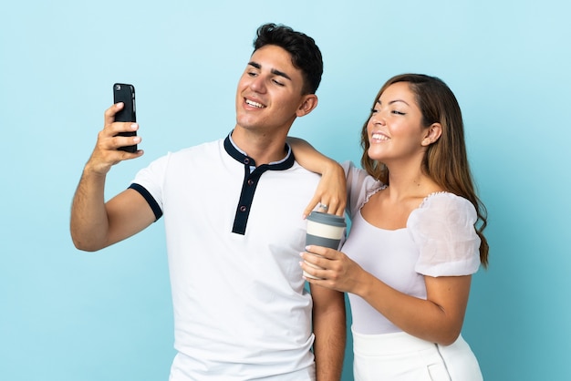 Jeune couple caucasien sur bleu faisant un selfie avec le mobile