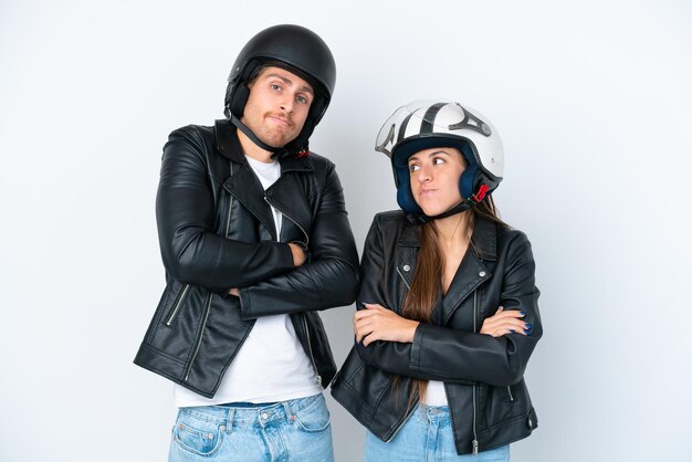 Jeune couple caucasien avec un casque de moto isolé sur fond blanc faisant des doutes geste tout en levant les épaules