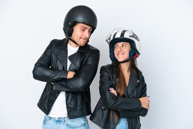 Jeune couple caucasien avec un casque de moto isolé sur fond blanc regardant par-dessus l'épaule avec un sourire