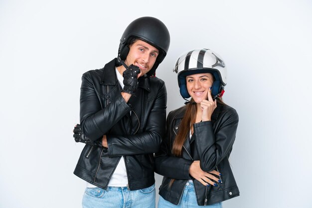 Jeune couple caucasien avec un casque de moto isolé sur fond blanc souriant avec une douce expression