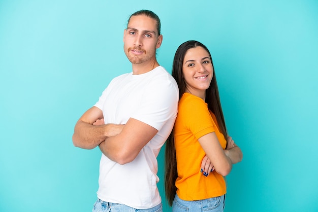 Jeune couple caucasien isolé sur fond bleu en gardant les bras croisés