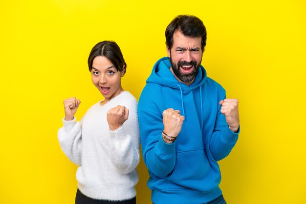 Jeune couple caucasien isolé sur fond jaune célébrant une victoire en position de vainqueur