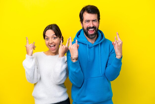 Jeune couple caucasien isolé sur fond jaune faisant un geste de rock