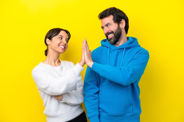 Jeune couple caucasien isolé sur fond jaune se cogner les mains