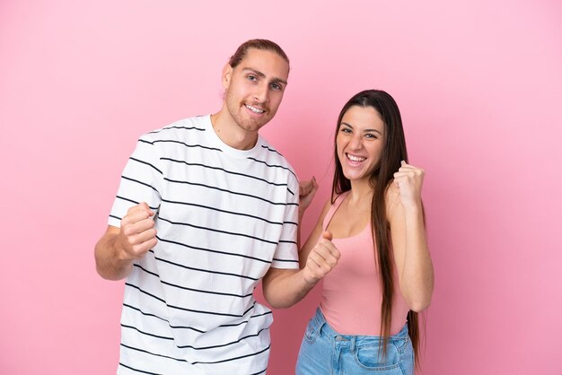 Jeune couple caucasien isolé sur fond rose célébrant une victoire en position de vainqueur