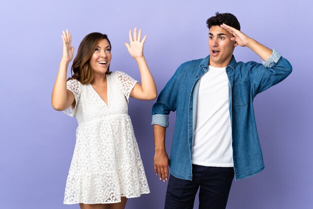 Jeune couple caucasien sur violet avec surprise et expression faciale choquée