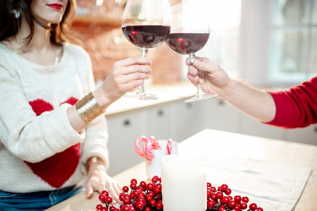 Jeune couple célébrant le Nouvel An avec des verres à vin dans la cuisine de leur appartement décoré, vue rapprochée