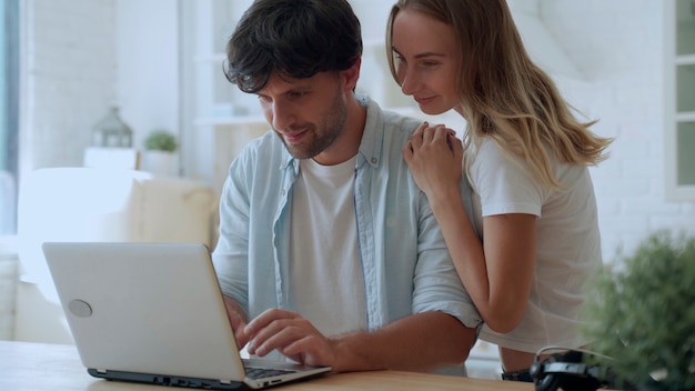 Jeune couple célébrant le succès, lisant de bonnes nouvelles par courrier électronique, regardant l'écran du portable, dans la cuisine à la maison