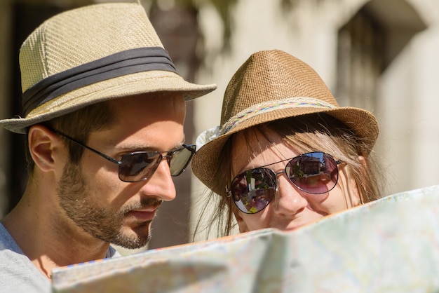 Un jeune couple avec des chapeaux, en regardant une carte