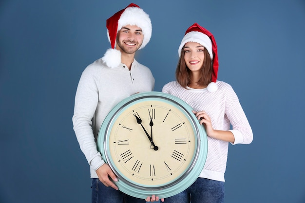 Jeune couple en chapeaux de Santa avec horloge sur l'espace colorimétrique. Concept de compte à rebours de Noël