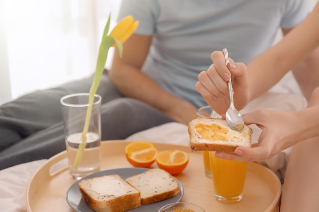 Jeune couple charmant prenant son petit déjeuner sur le lit