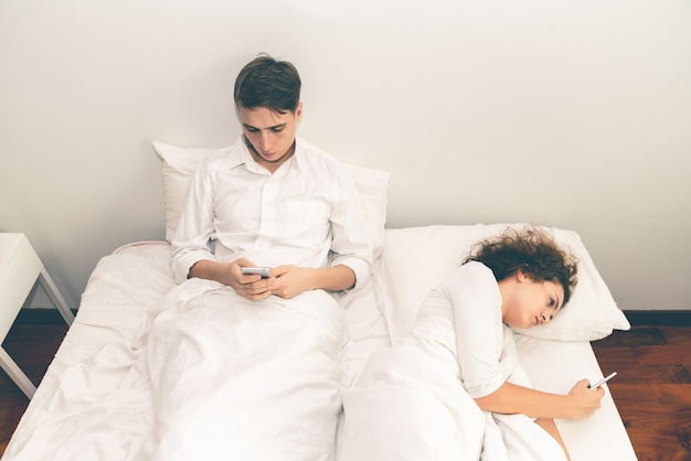 Jeune couple cherche smartphone sur le lit