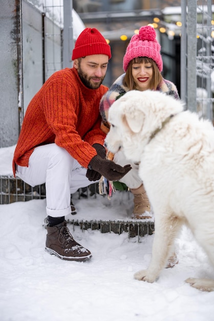 Jeune couple avec chien sur un porche de leur maison en hiver